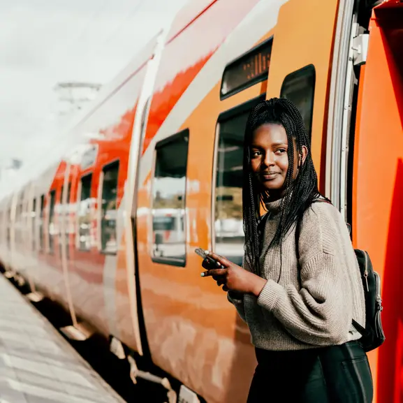 Ung kvinna med flätor står vid ett orange tåg på en solig dag