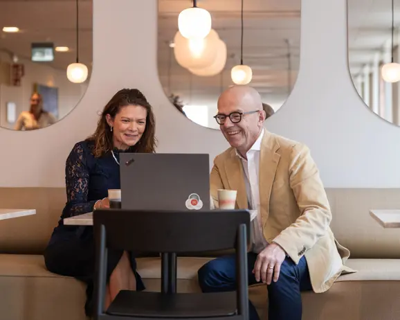 Två personer i affärsmöte vid ett bord, leende medan de tittar på en bärbar dator i ett modernt kontorsutrymme