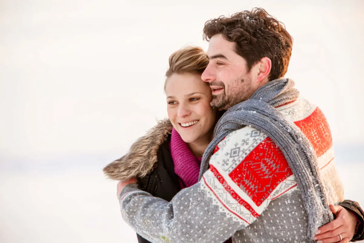 Ungt par som kramas utomhus i vintermiljö, klädda i varma vinterkläder