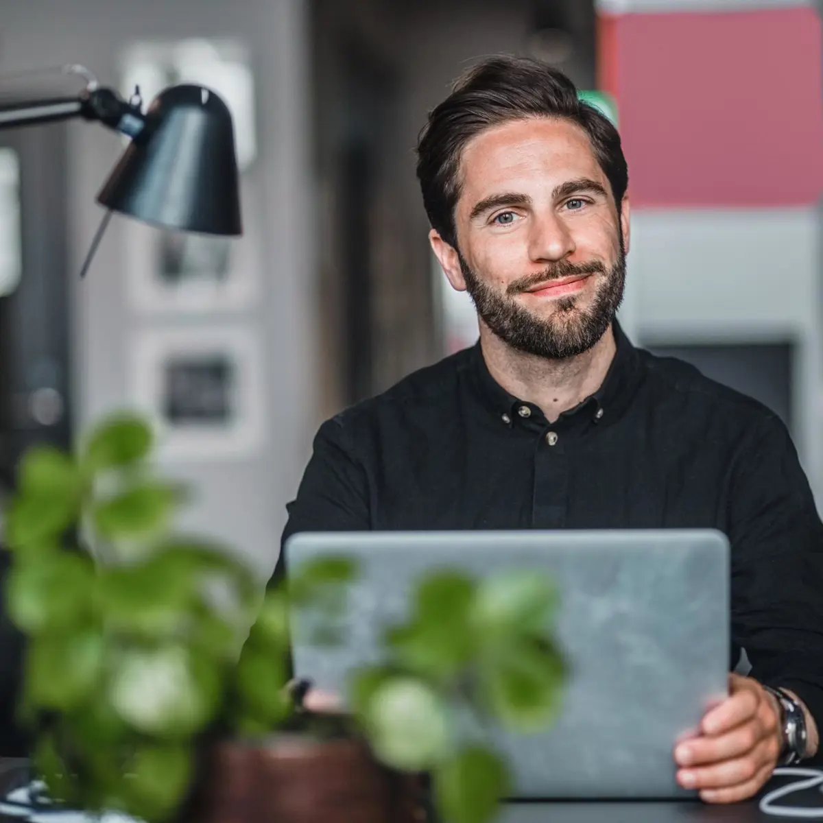 Man som arbetar på en bärbar dator vid ett skrivbord med en skrivbordslampa och gröna växter